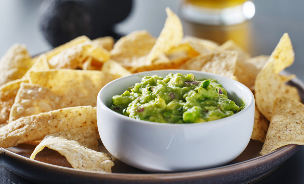 plate of corn tortilla chips with guacamole dip close up