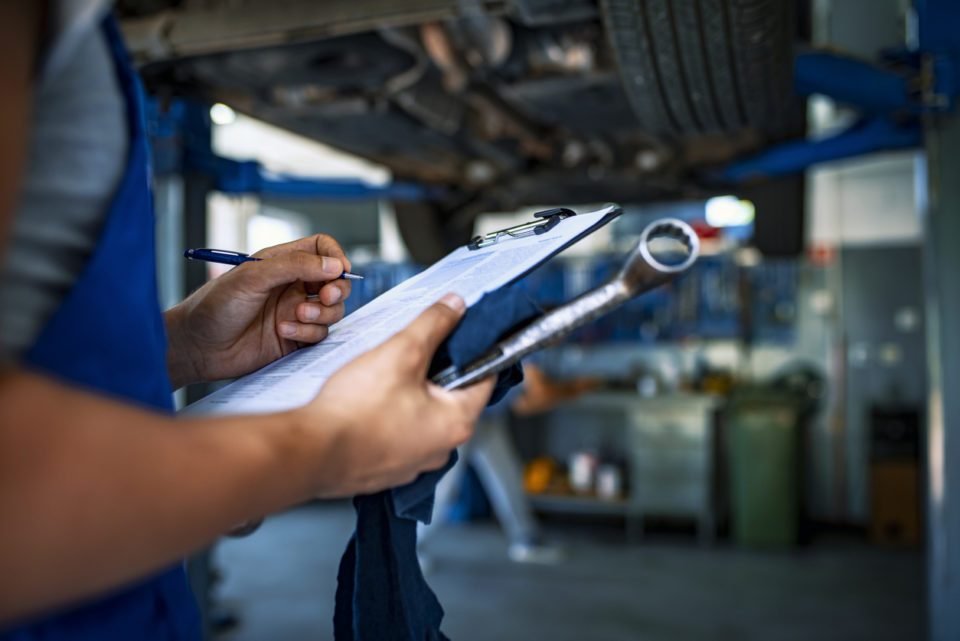 Mechanic under car preparing checklist in workshop.