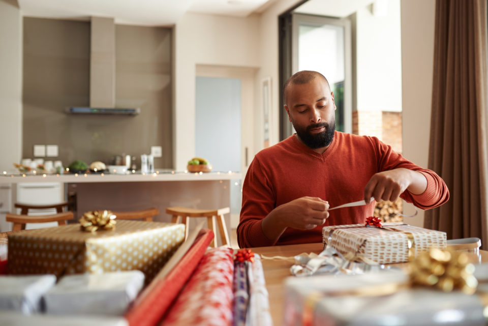 Shot of a young man wrapping Christmas presents at home