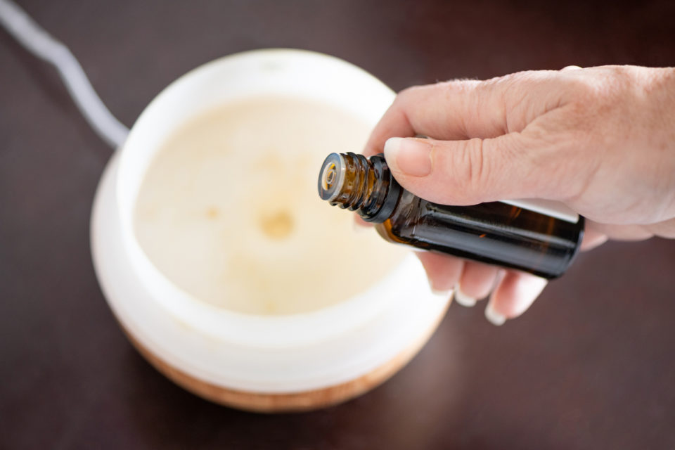 Woman’s hand putting essential oil into a plugged in diffuser