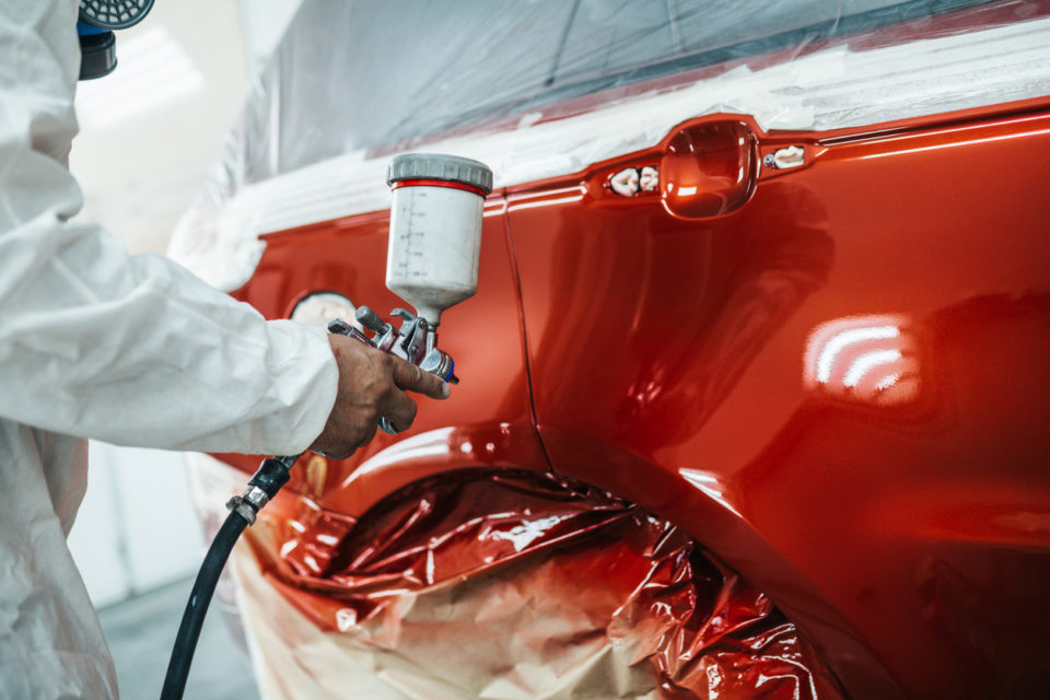 Man with protective clothes and mask painting car using spray compressor.