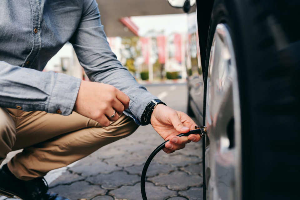 Close up of man crouching at the gas station and inflating tire.