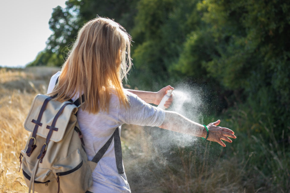 Woman applying mosquito repellent on hand during hike in nature.