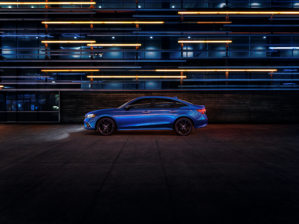 A blue 2022 Honda Civic Sedan driving at night, blurred lights in the background.