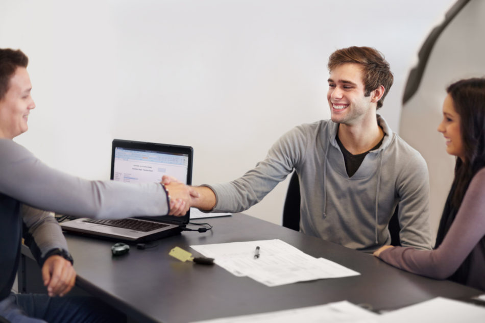 Young couple in a car salesman's office signing paperwork for a new car