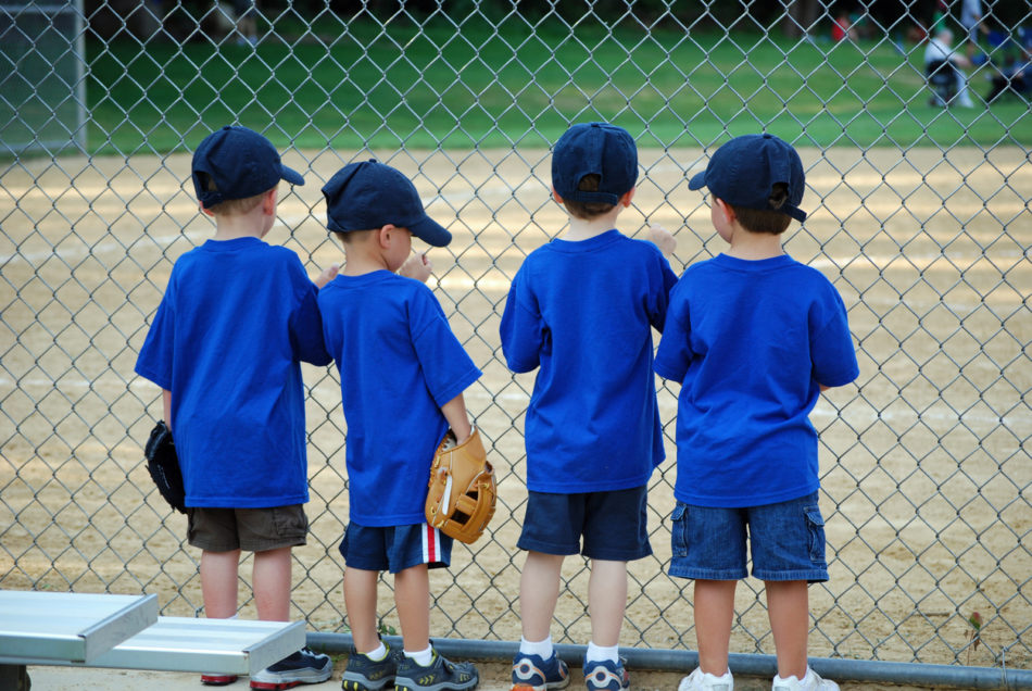 4 little boys waiting at the fence for their baseball game to begin