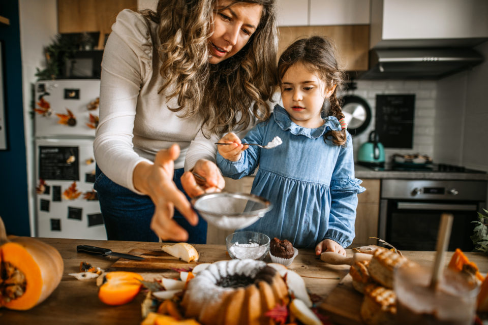Mother and daughter in kitchen dusting cake with powdered sugar
