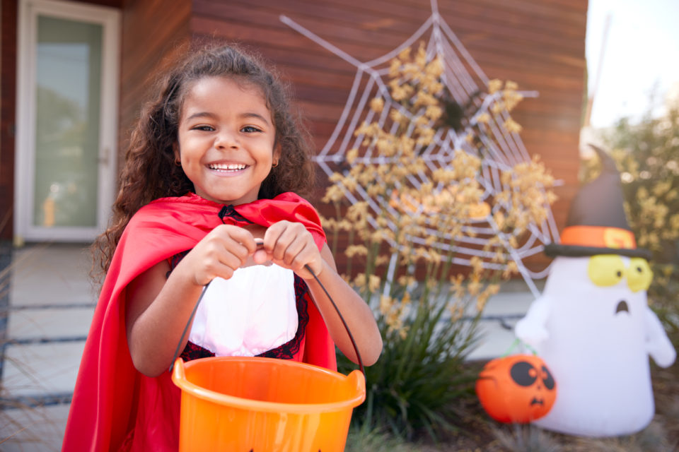 Portrait Of Girl Wearing Fancy Dress Outside House Collecting Candy For Trick Or Treat