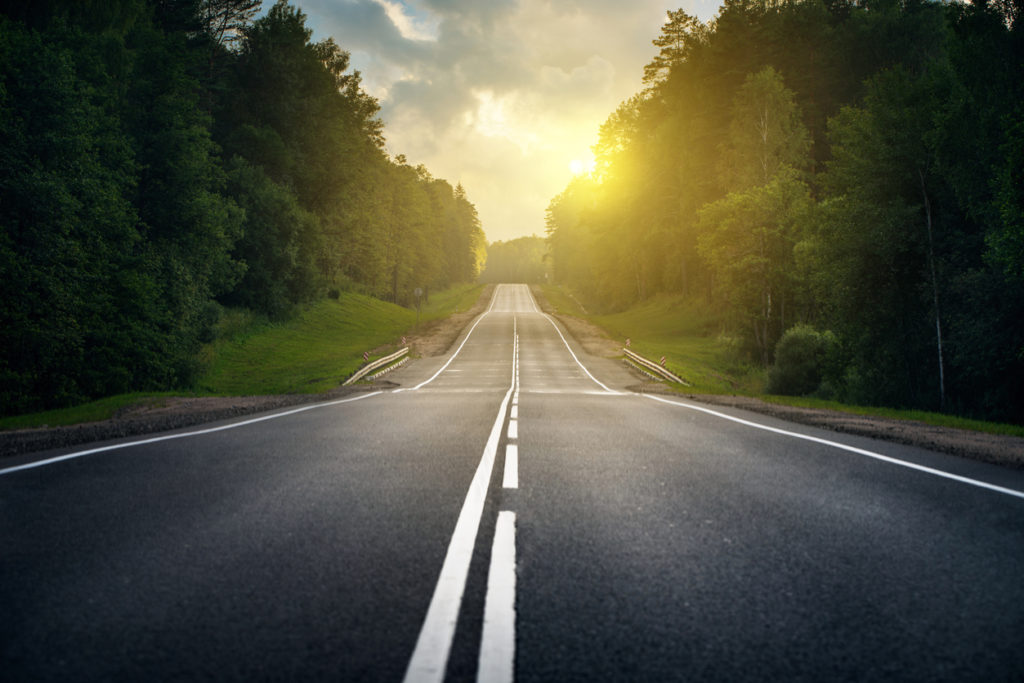 open road through forest at sunrise