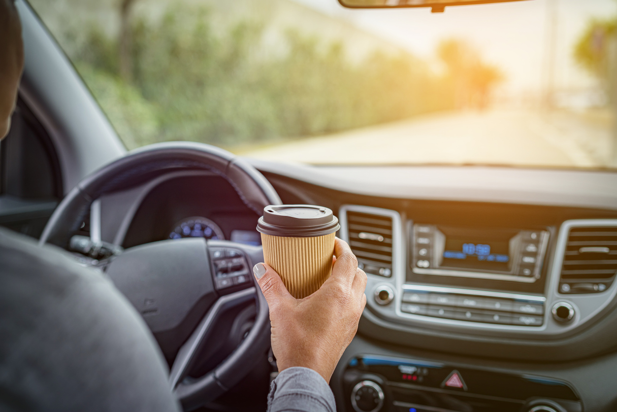 Woman holding disposable coffee cup while driving