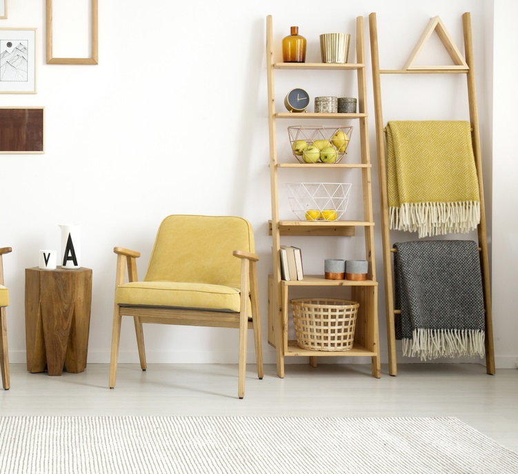 Wooden stool between yellow armchairs near white cupboard in living room interior with posters